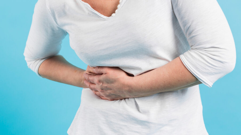 Persona seduta in casa che appoggia le mani sull’addome con espressione pensierosa