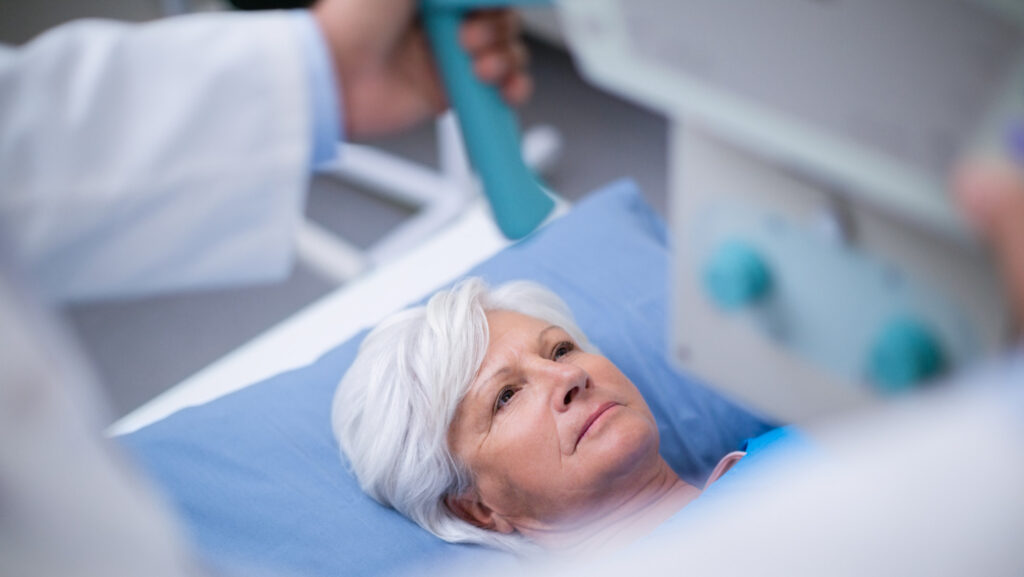 Operatore socio-sanitario che assiste una persona prima di un intervento chirurgico in ambiente ospedaliero.