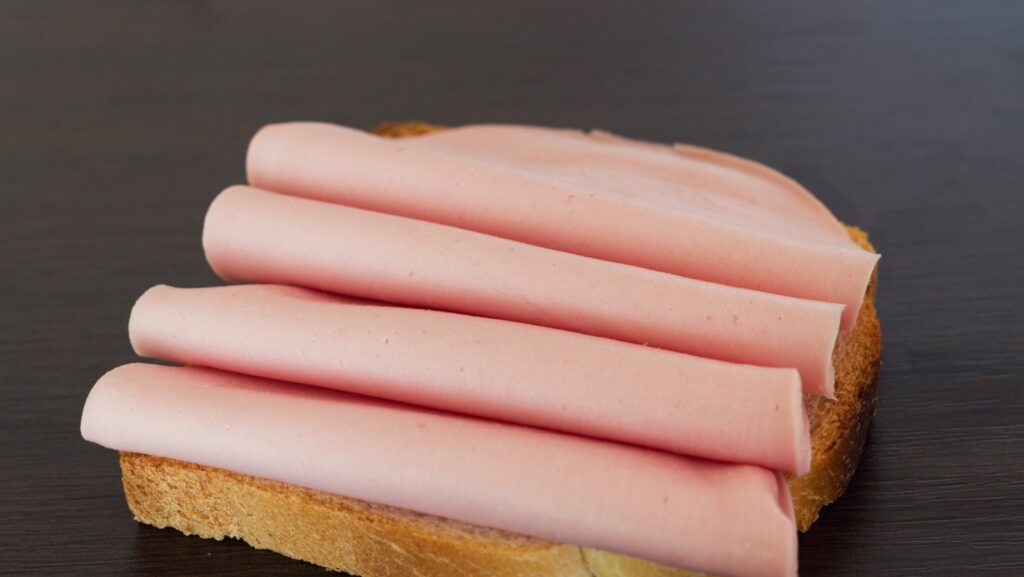 Prosciutto cotto affettato su un piatto in una cucina domestica, pronto per un pasto quotidiano.
