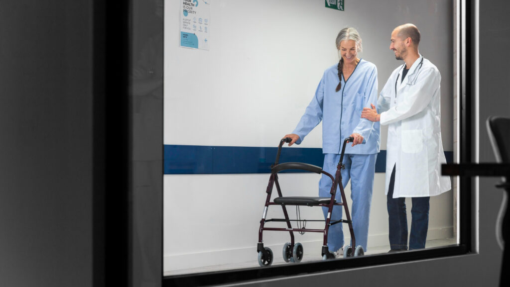 Operatore socio-sanitario che osserva con attenzione una persona assistita in un reparto ospedaliero.