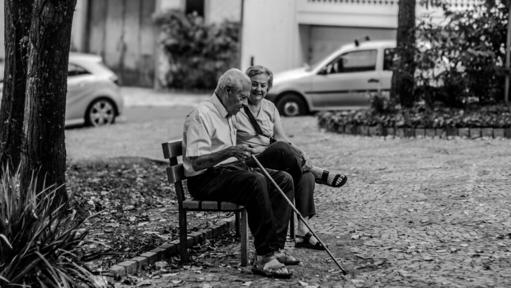 Nell'immagine due anzieni seduti su una panchina, pensierosi. Immagine in bianco e nero.